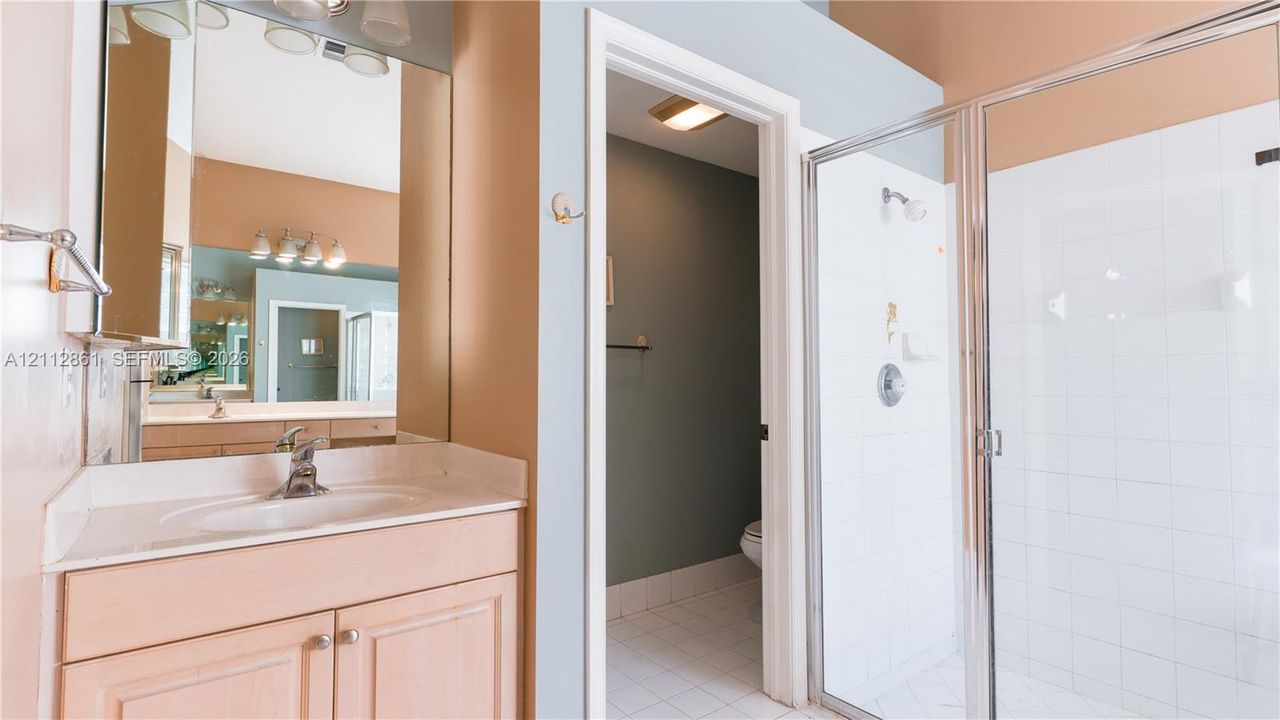 Bathroom featuring a light-toned wood vanity, integrated sink, oversized wall-mounted mirror, and a walk-in shower enclosed by a chrome-framed glass door