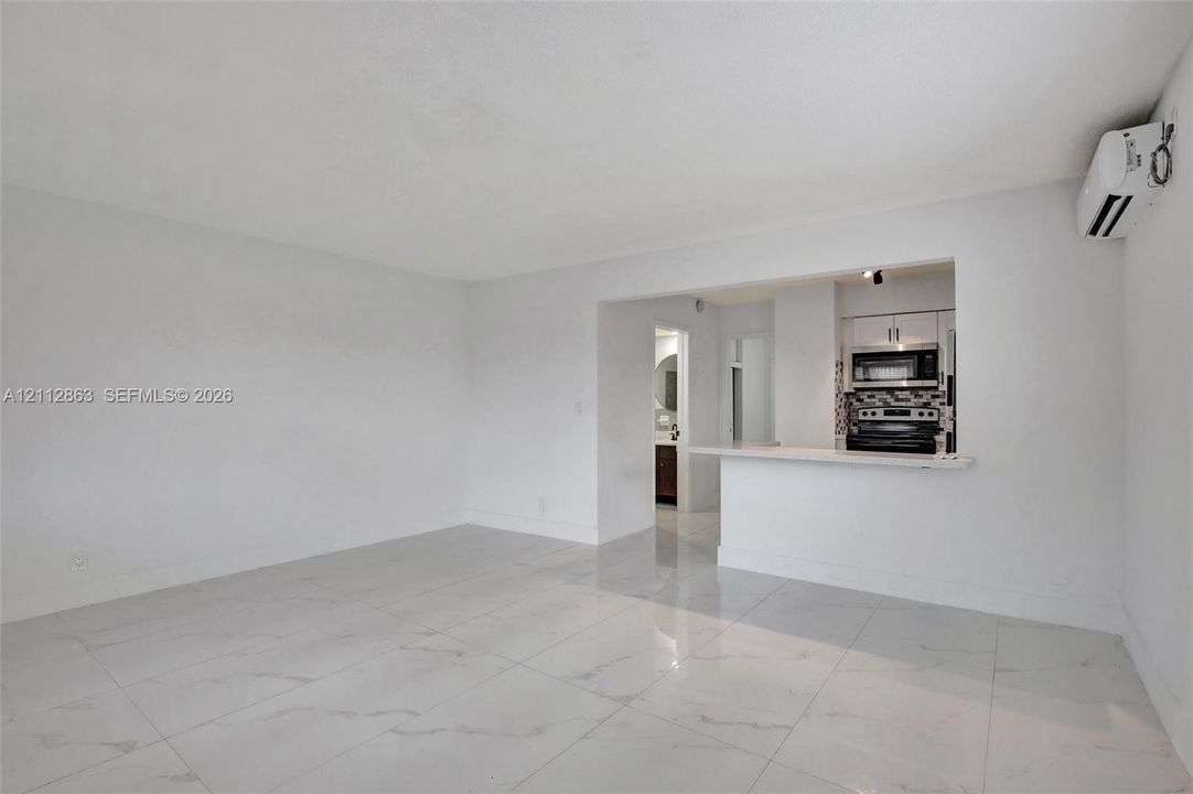 Open-concept interior featuring large-format tile flooring, a breakfast bar, and a wall-mounted ductless air conditioning unit