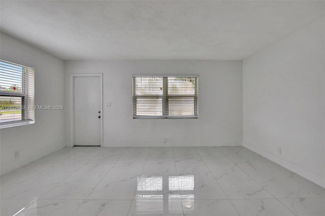 Open-concept room featuring large-format tile flooring with a veined pattern, neutral wall finishes, and multiple windows with horizontal blinds