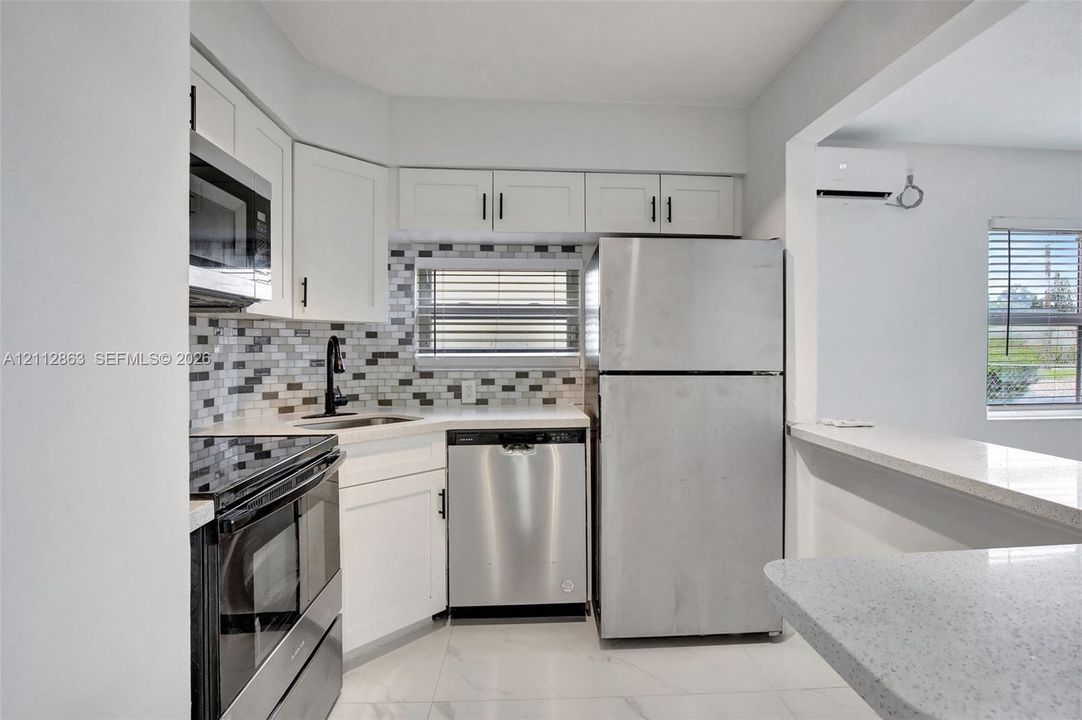 Kitchen featuring white Shaker-style cabinetry, stainless steel appliances, multi-toned mosaic tile backsplash, solid-surface countertops, and tile flooring