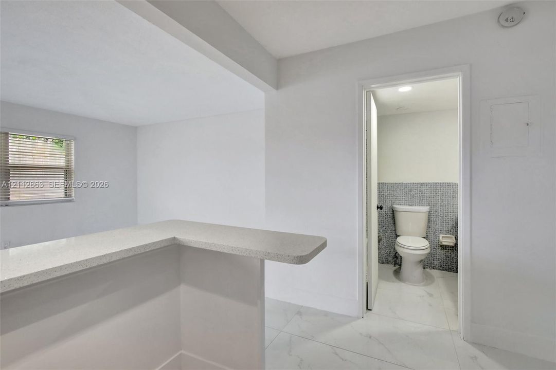Neutral-toned kitchen counter with a matte finish, white porcelain tile flooring, and a bathroom featuring mosaic tile wall accents