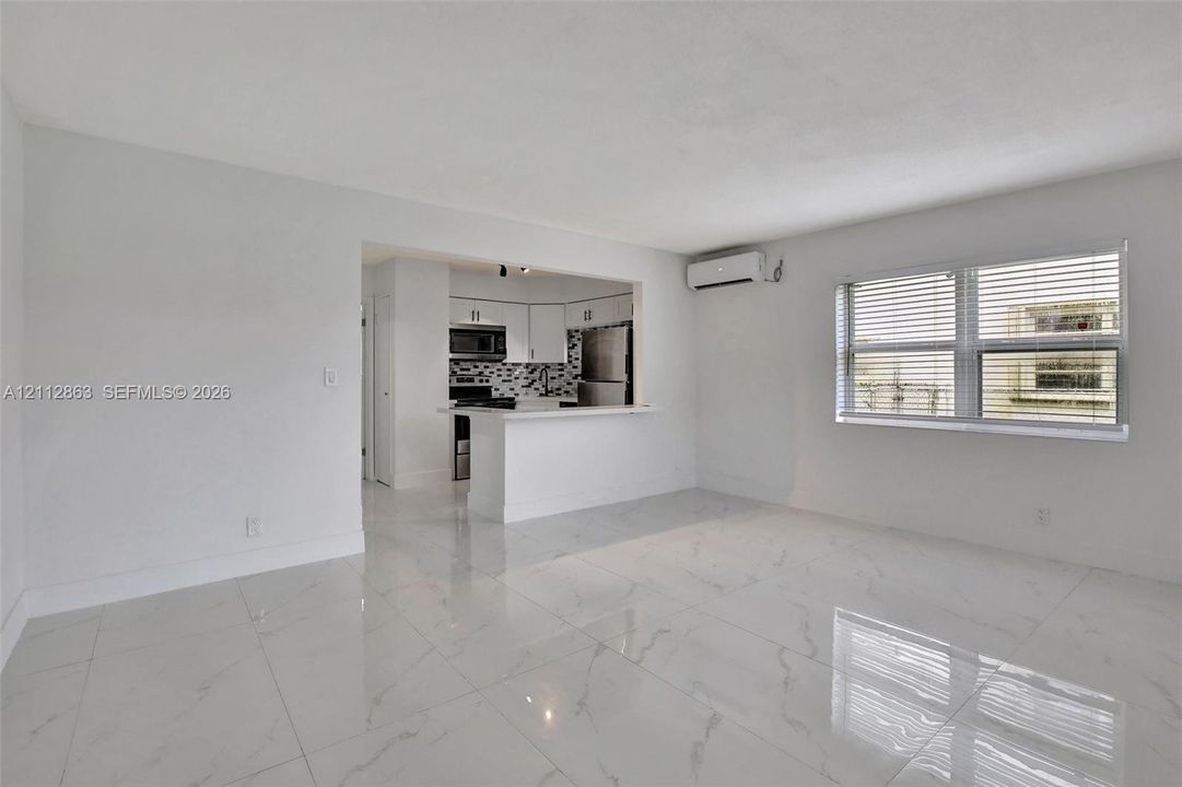 Polished stone-finish tile flooring, kitchen pass-through with breakfast bar, stainless steel appliances, patterned backsplash, and wall-mounted ductless climate control system