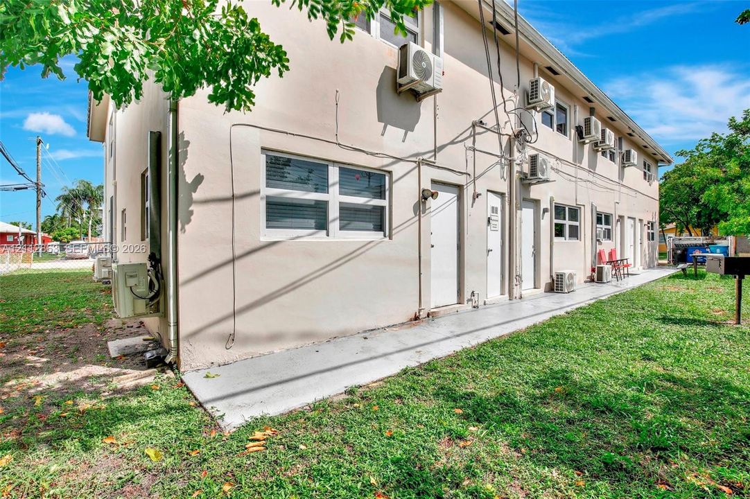 Stucco exterior building featuring multiple wall-mounted air conditioning units, sliding windows, and a poured concrete walkway
