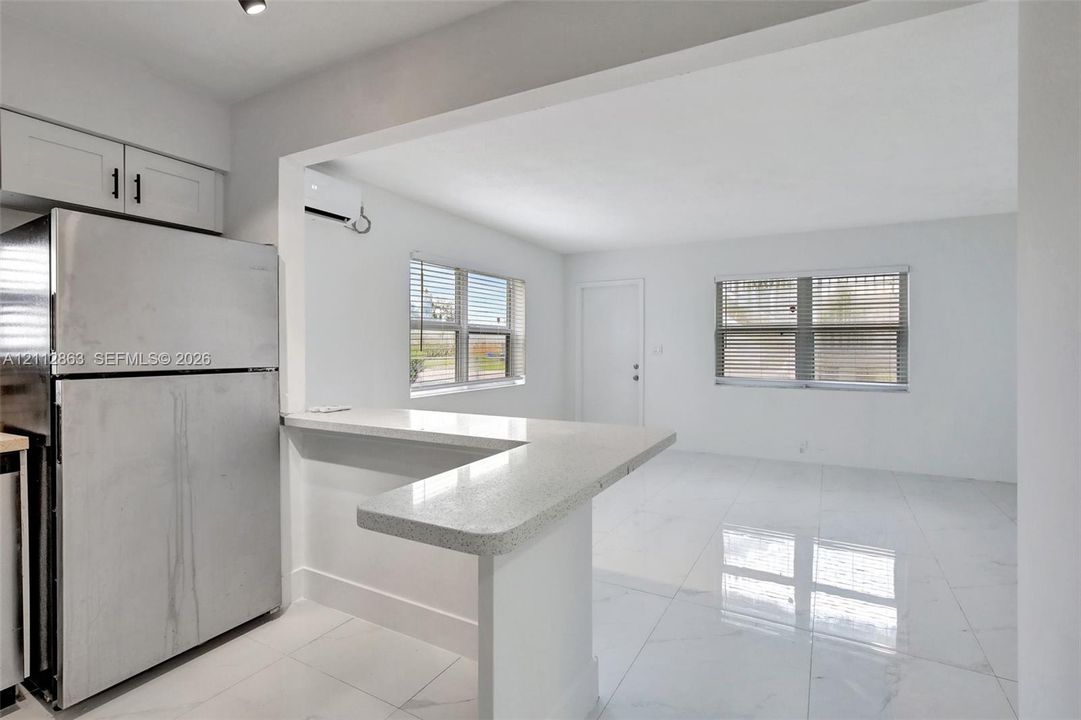 Kitchen featuring an L-shaped breakfast bar with quartz countertop, high-gloss tile flooring, stainless steel refrigerator, and white cabinetry
