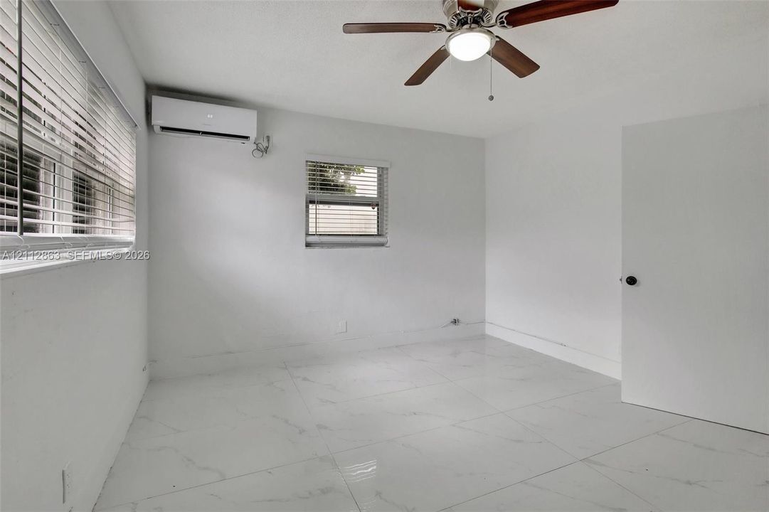 Large-format polished tile flooring, wall-mounted ductless air conditioning unit, ceiling fan with integrated lighting, and horizontal window blinds