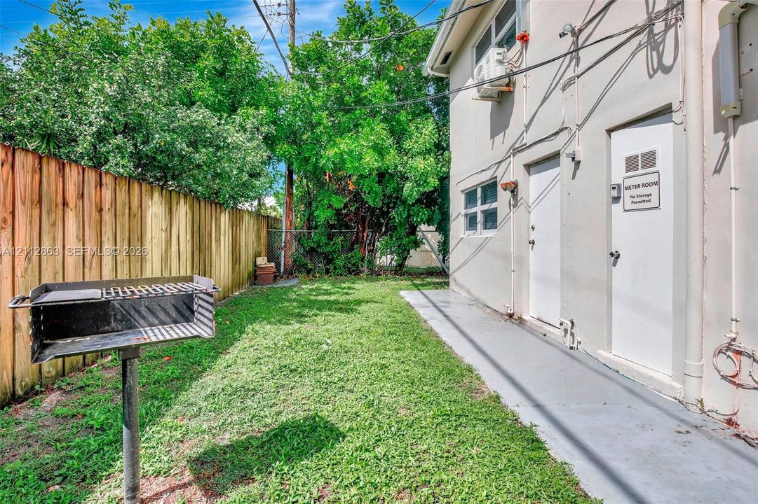 Exterior side yard featuring a wood-panel fence, a stationary metal grill, and a concrete walkway