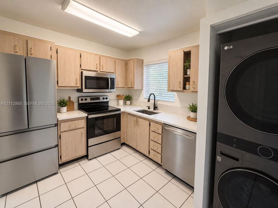 Kitchen featuring light-finish wood cabinetry, solid-surface countertops, stainless steel appliances, a deep basin sink with a matte black faucet, and ceramic tile flooring
