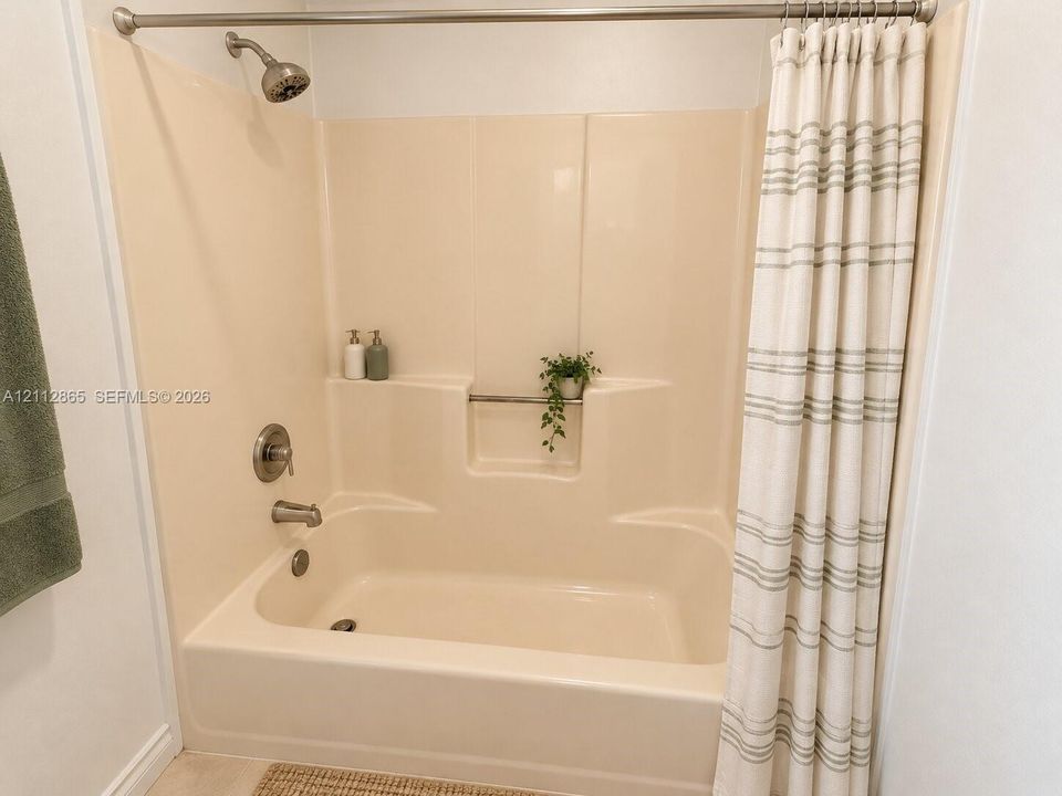 Bathtub and shower combination featuring a molded surround, integrated storage niche, and brushed nickel hardware