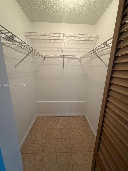 Walk-in closet featuring floor-to-ceiling white walls, ceramic tile flooring, and integrated white wire shelving