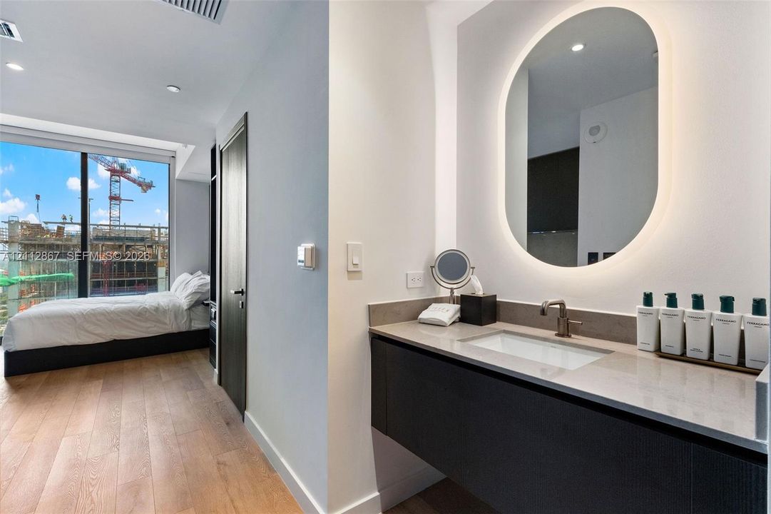 Modern floating vanity with a neutral-tone countertop, undermount sink, and metallic faucet, complemented by a backlit oval wall mirror and wood-finish flooring