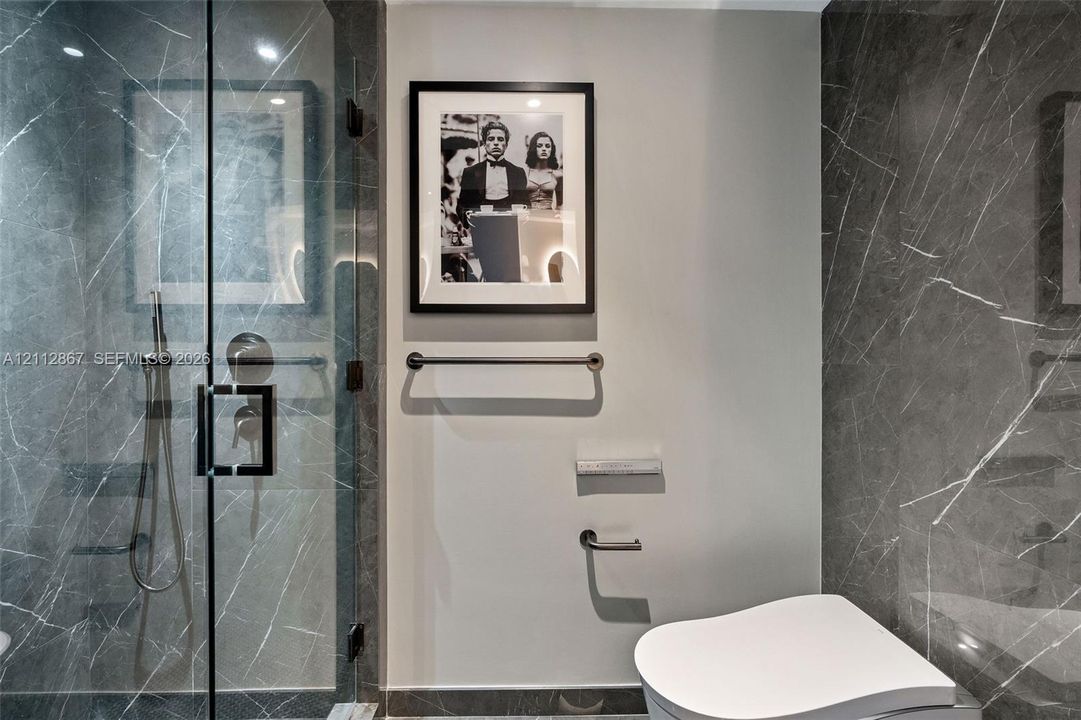 Shower stall featuring full-height stone-finish wall tile, a frameless glass door, and a handheld spray fixture, complemented by polished metal hardware and fixtures