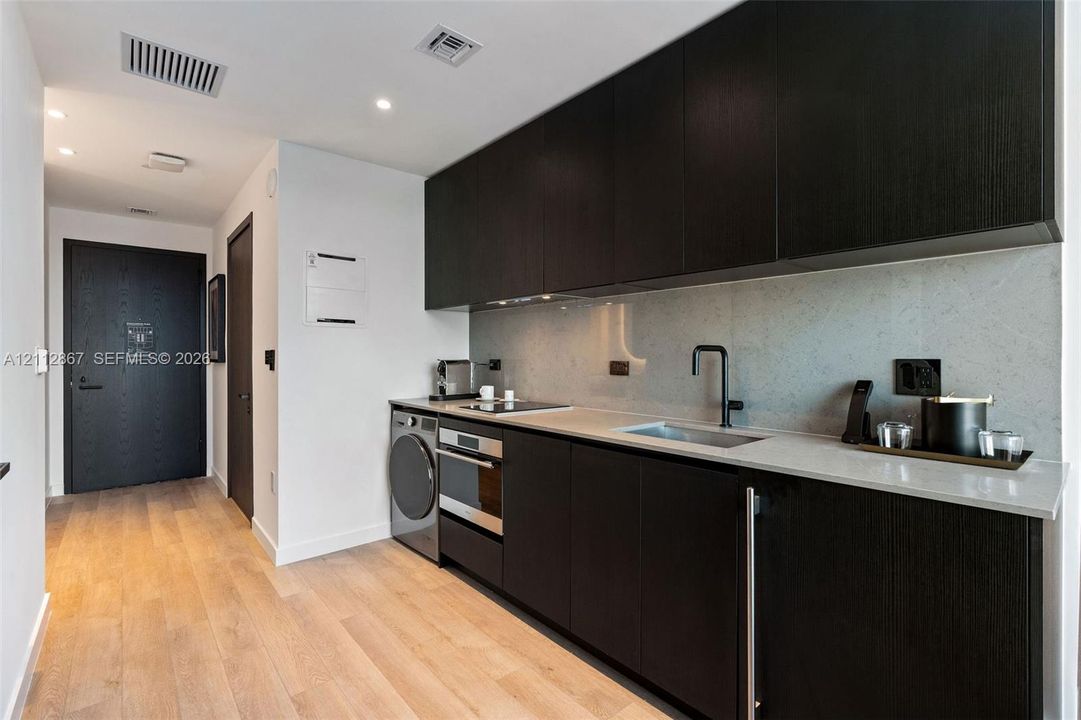 Kitchen featuring dark wood-finish cabinetry, solid surface countertops, a full-height stone backsplash, integrated stainless steel appliances, and wood-finish flooring