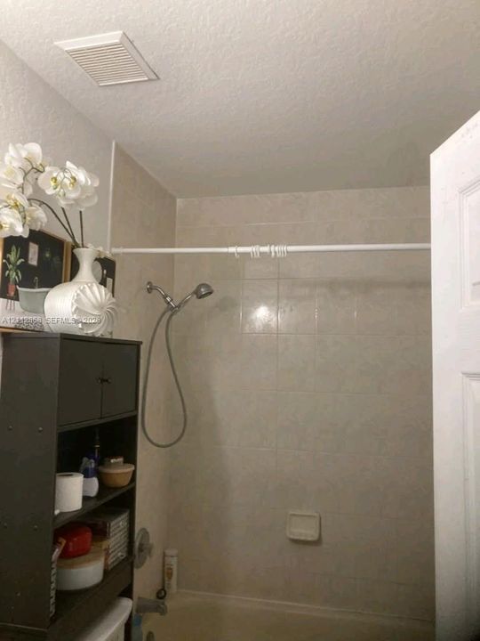 Bathtub and shower combination featuring neutral ceramic wall tile, a hand-held shower fixture, and a built-in recessed soap dish
