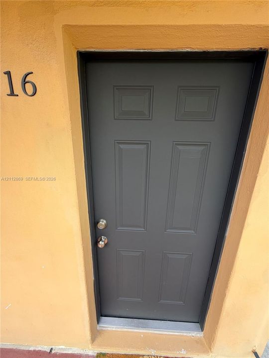 Six-panel exterior door featuring a dark gray finish, metallic hardware, and a recessed threshold set against a textured stucco wall