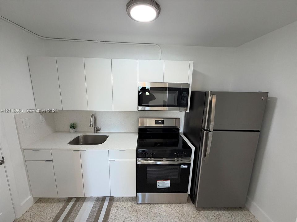 Kitchen featuring white flat-panel cabinetry, stainless steel appliances, and a single-basin undermount sink