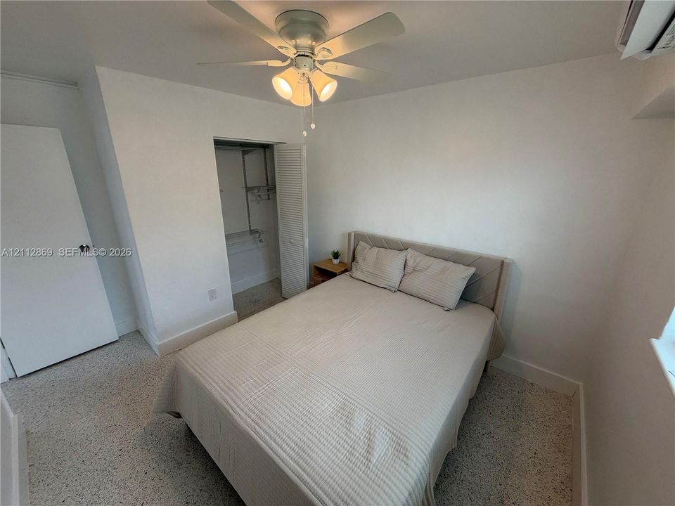 Terrazzo flooring, multi-blade ceiling fan with integrated lighting, reach-in closet with bi-fold louvered door, and wall-mounted climate control unit