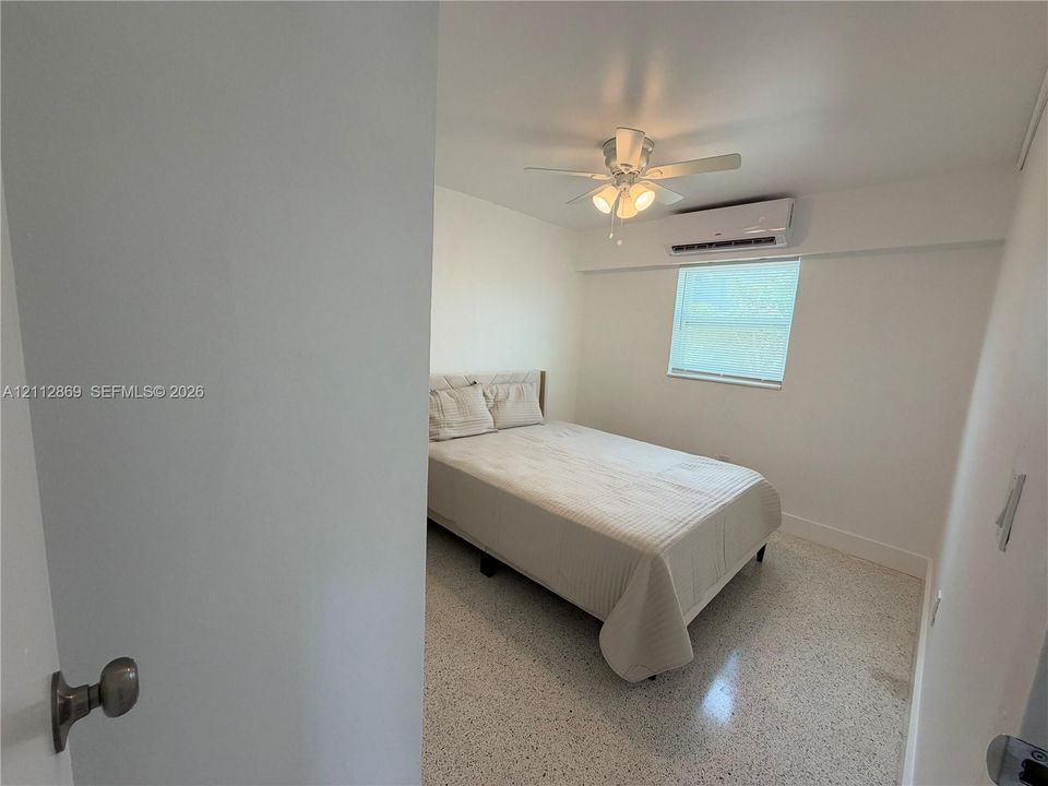 Neutral-toned interior featuring terrazzo flooring, ceiling fan with integrated lighting, and wall-mounted ductless air conditioning unit