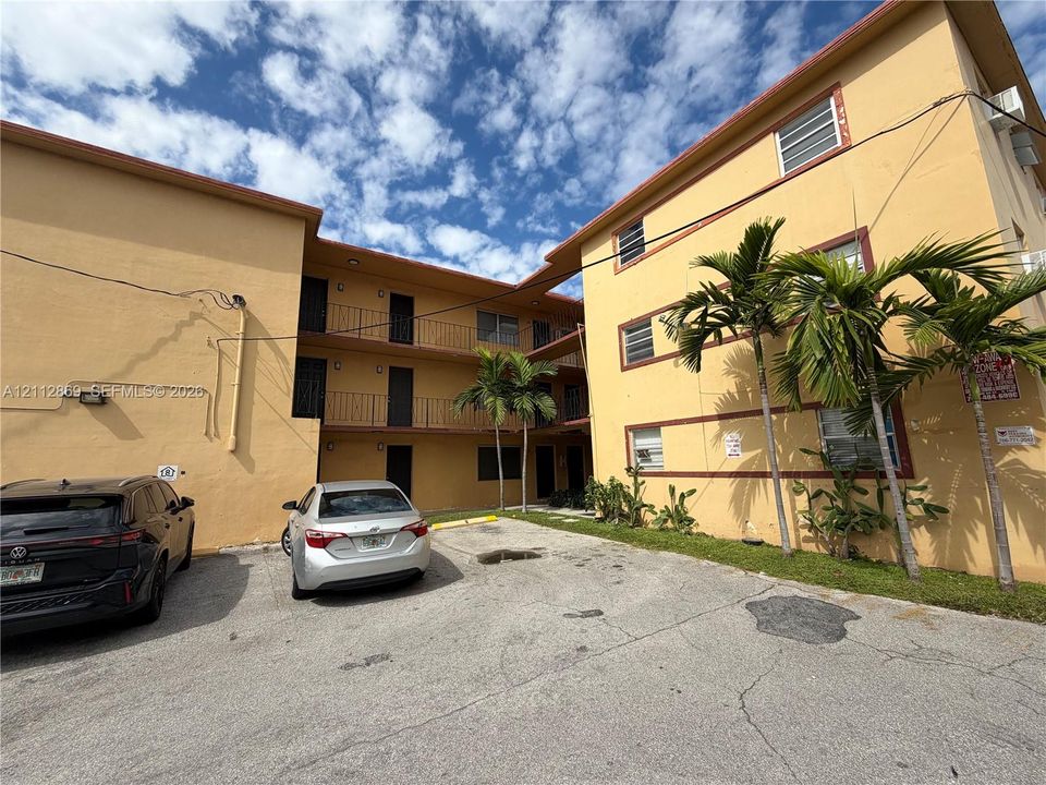 Three-story stucco exterior featuring covered balconies, dedicated surface parking, and mature palm trees