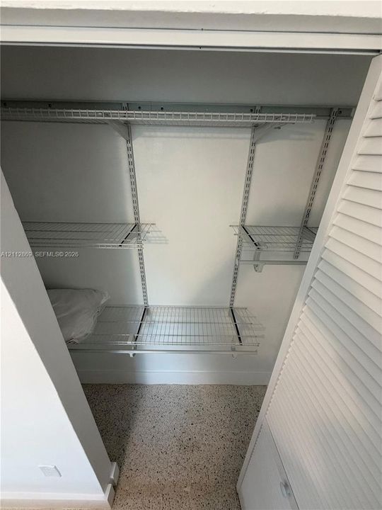 Storage closet featuring adjustable white wire shelving, a hanging rod, and louvered swinging doors