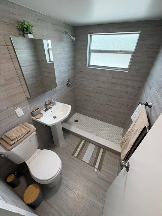 Bathroom featuring horizontal wall tiling, pedestal sink, shower with white hexagonal floor tile, and a rectangular mirror