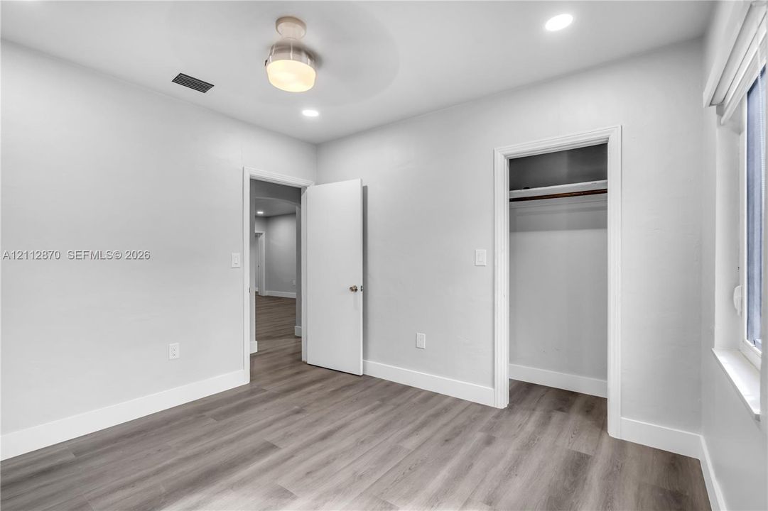 Neutral-toned interior space featuring wood-finish flooring, recessed lighting, a modern ceiling-mounted light fixture, and a reach-in closet
