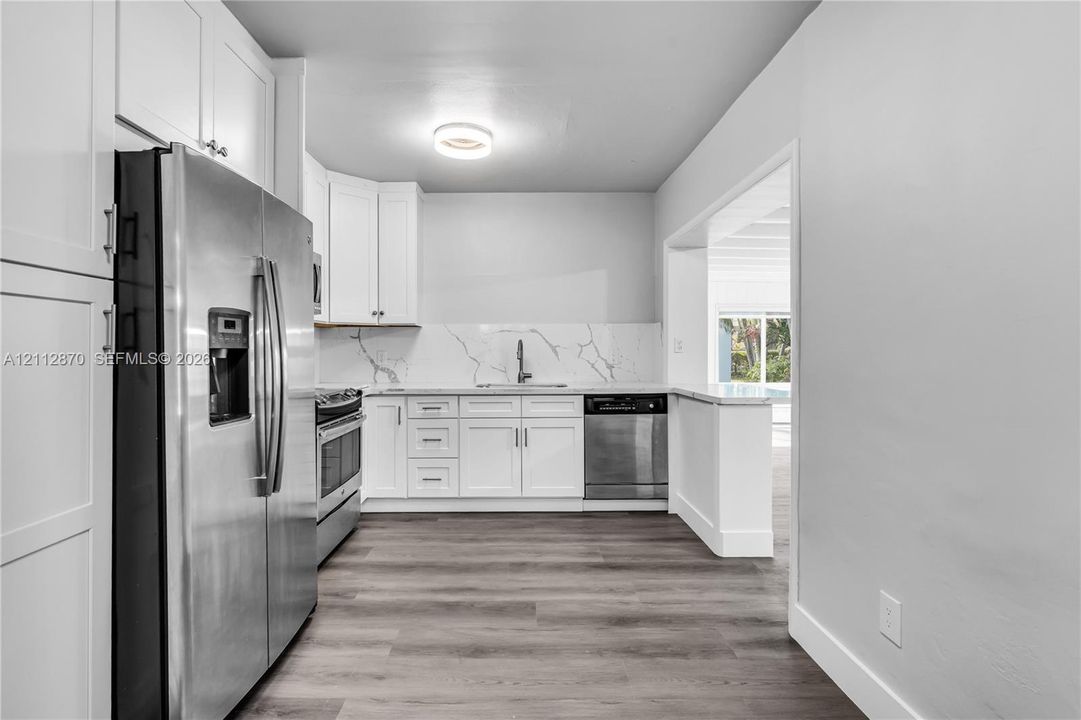 Kitchen featuring white shaker-style cabinetry, stone-patterned backsplash, stainless steel appliances, and wood-finish flooring