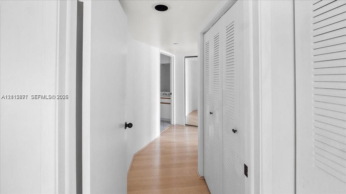 Hallway featuring wood-finish flooring, white walls, and built-in closet cabinetry with louvered doors