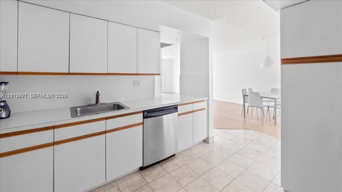 Kitchen featuring white cabinetry with wood trim, solid-surface countertops, stainless steel undermount sink, and stainless steel dishwasher