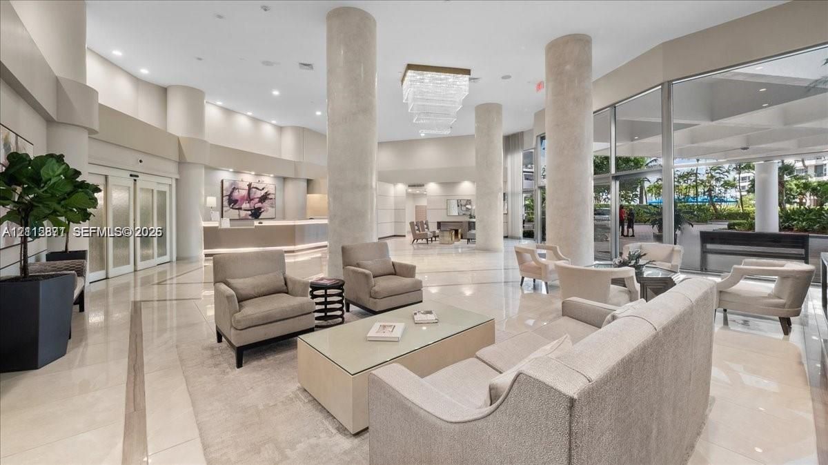 Grand lobby featuring high ceilings, polished stone flooring, architectural columns, expansive floor-to-ceiling glass windows, and a multi-tiered crystal chandelier