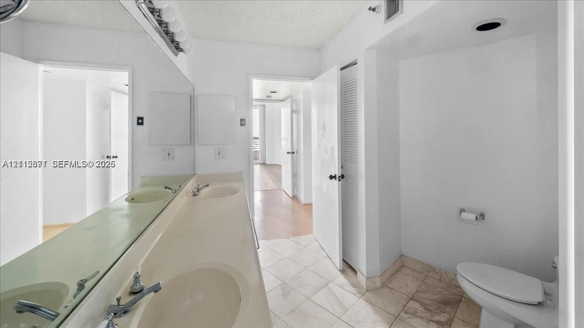 Double vanity featuring an integrated countertop with dual basins, large wall-to-wall vanity mirror, and ceramic tile flooring
