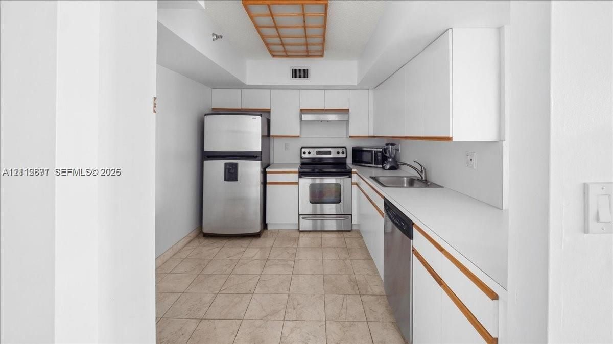 Kitchen featuring flat-panel white cabinetry with wood-finish trim, stainless steel appliances, solid-surface countertops, and tiled flooring