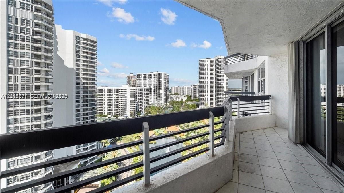 Covered balcony featuring tile flooring and horizontal metal railings overlooking high-rise structures