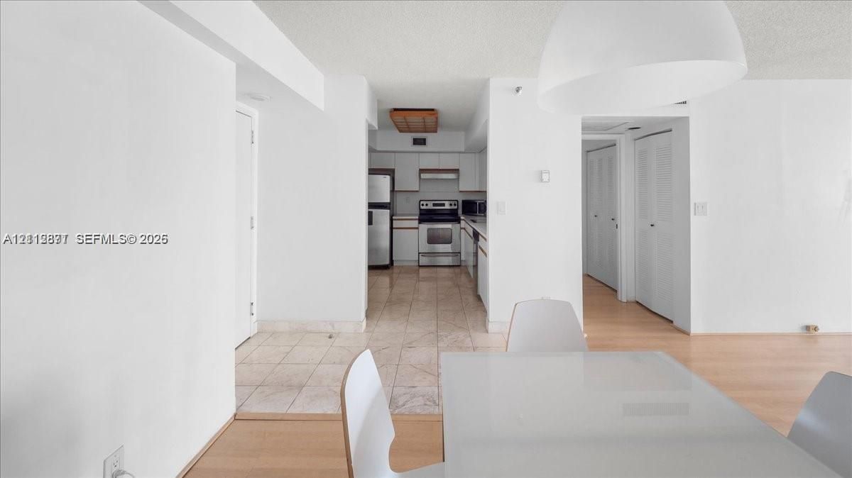Kitchen featuring white cabinetry, stainless steel appliances, and tile flooring, paired with wood-finish flooring and a minimalist overhead pendant light
