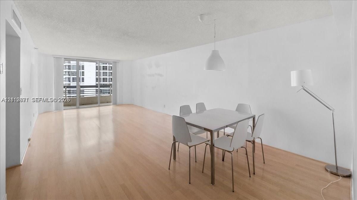 Open-concept floor plan featuring wood-finish flooring, sliding glass balcony doors, and a pendant-mounted light fixture