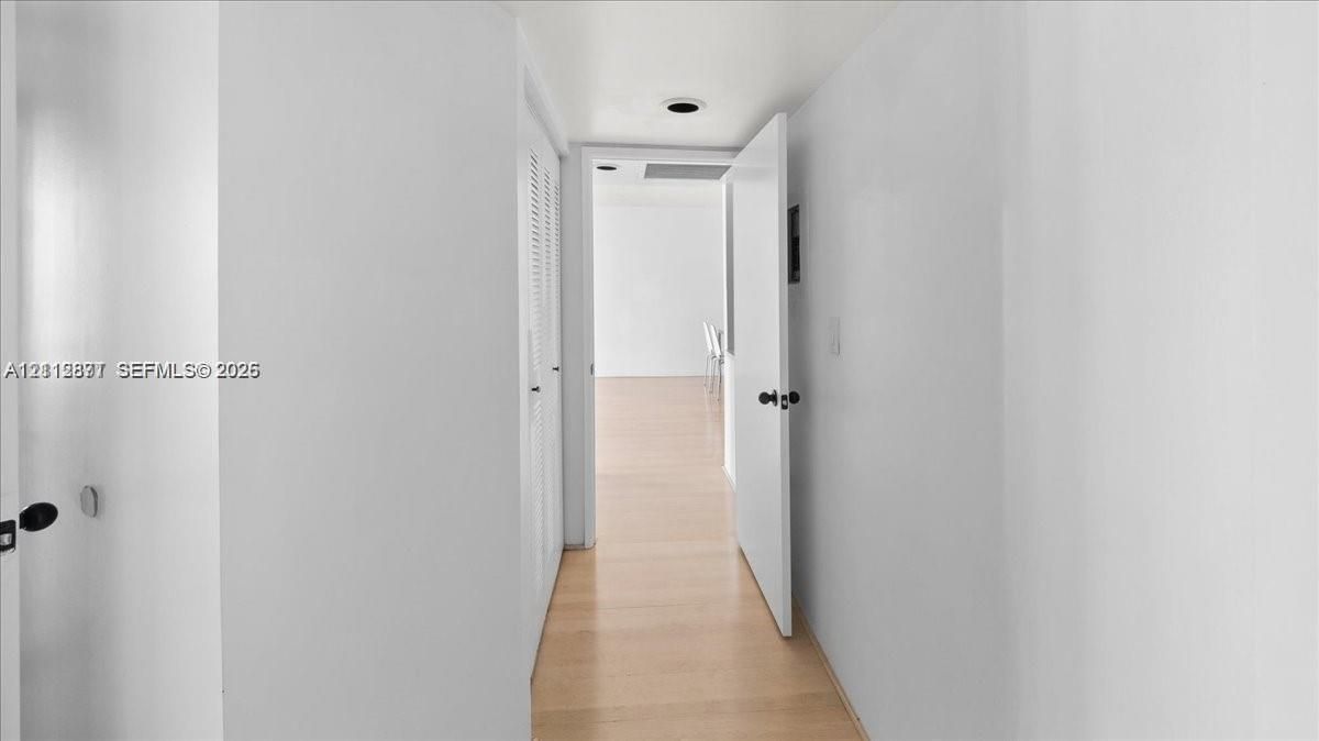 Hallway featuring wood-finish flooring, white walls, and built-in louvered closet doors with matte black hardware