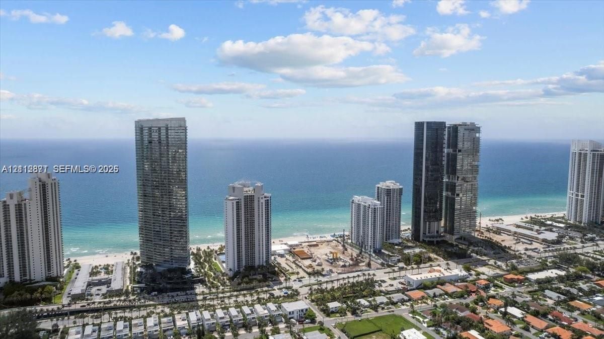 Aerial perspective of coastal high-rise towers positioned along an expansive sandy beach and ocean shoreline