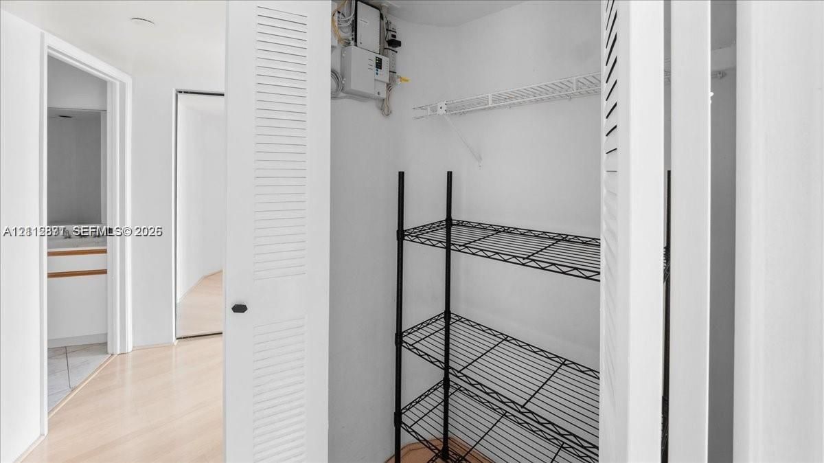 Storage closet featuring white louvered doors and an installed white wire shelf, set against wood-finish flooring