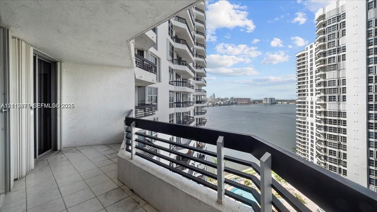 Covered balcony featuring tile flooring and a black metal railing overlooking the water
