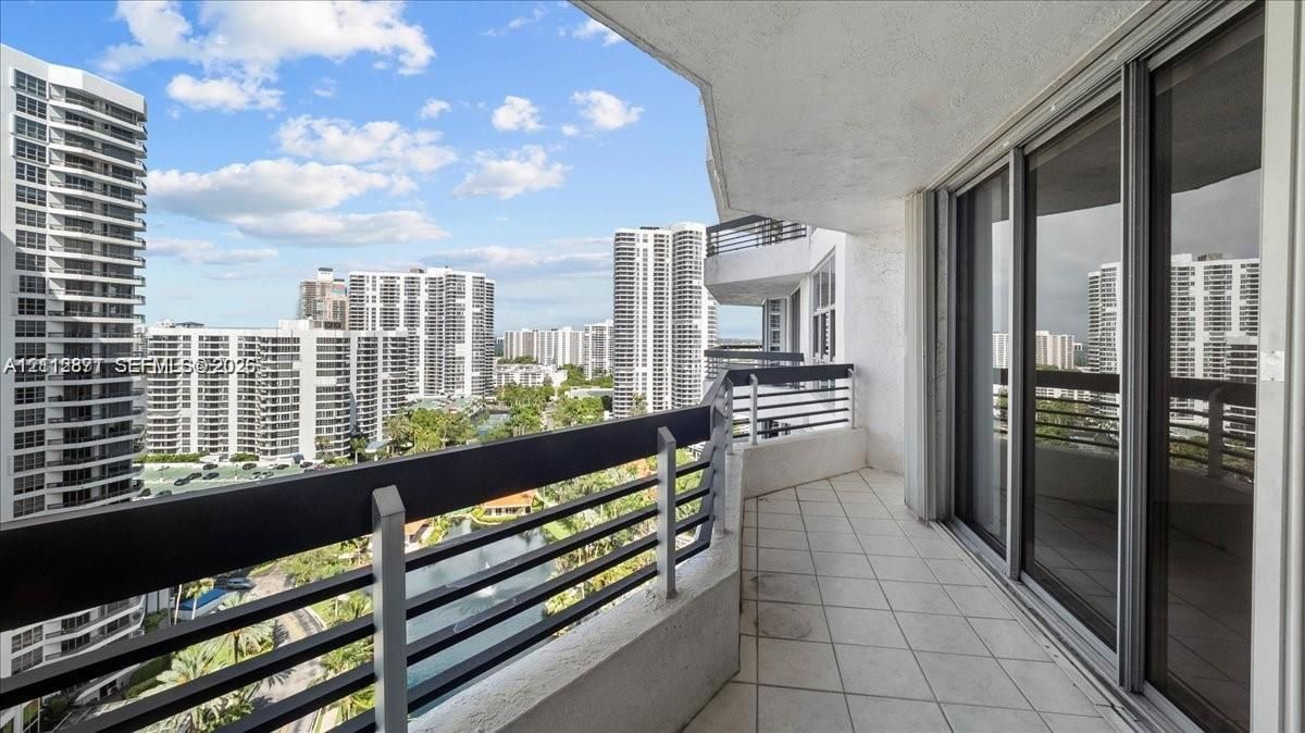 Covered balcony featuring white tile flooring, black metal railing, and floor-to-ceiling sliding glass doors