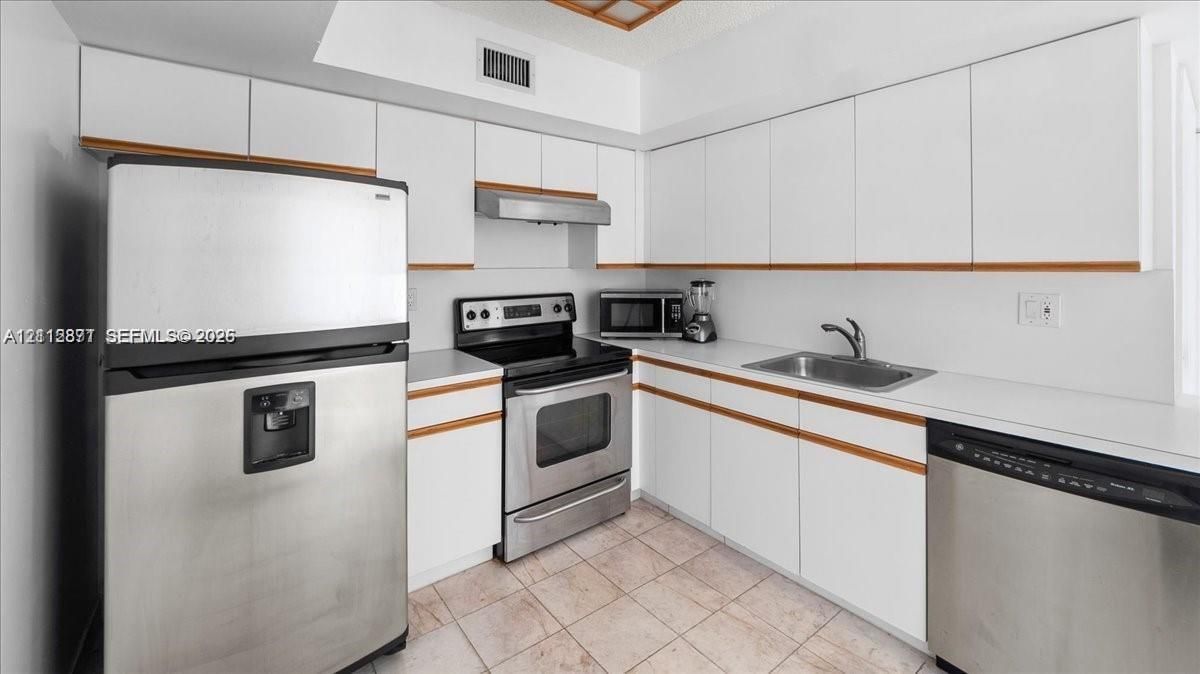Kitchen featuring white flat-panel cabinetry with wood trim, stainless steel appliances, solid surface countertops, a stainless steel sink with a goose-neck faucet, and tile flooring
