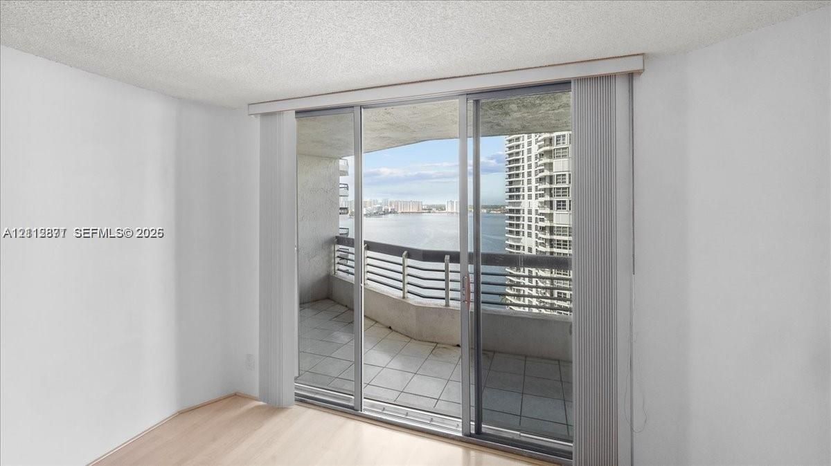 Sliding glass doors opening to a concrete balcony with metal railings, wood-finish flooring, and water frontage