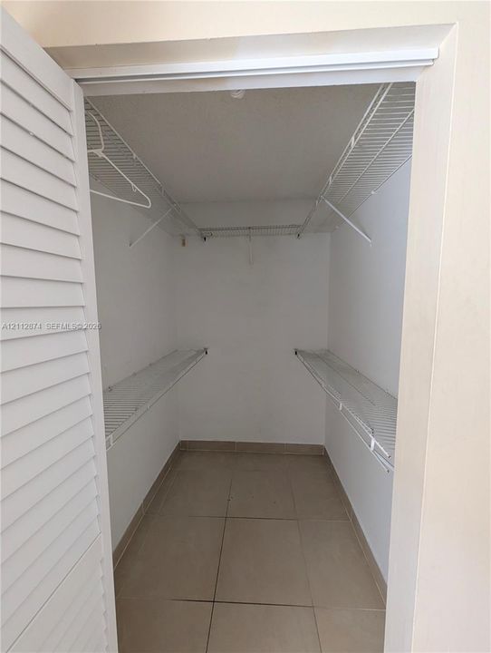 Storage closet featuring louvered bi-fold doors, white wire shelving, and large-format tile flooring