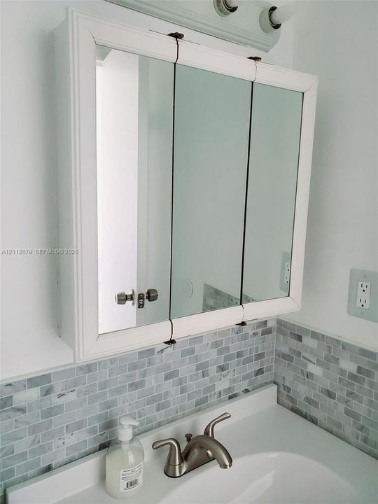 Tri-view medicine cabinet with white frame, white vanity top with integrated basin, polished metal double-handle faucet, and mosaic tile backsplash