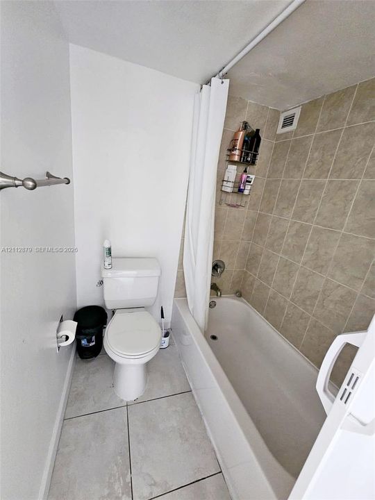 Bathroom featuring a white porcelain toilet, bathtub with a shower head, and neutral-toned wall and floor tile