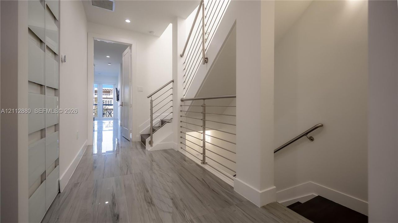 Staircase featuring horizontal metal balustrades, recessed ceiling lighting, and wood-finish tile flooring