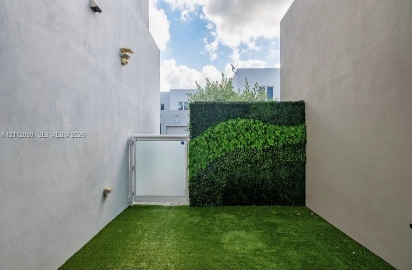 Enclosed courtyard featuring smooth stucco walls, artificial turf, an integrated vertical garden wall, and a frosted glass pedestrian gate