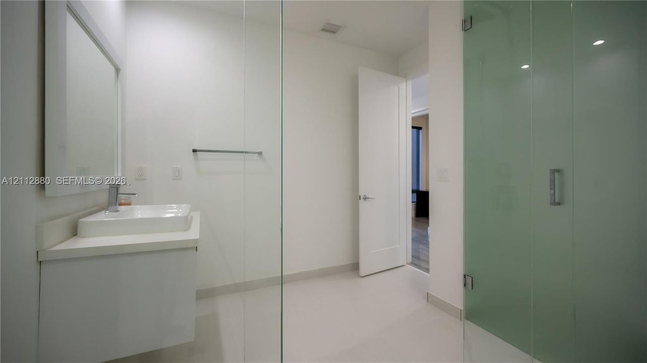 Bathroom featuring a floating vanity with a rectangular vessel sink, wall-mounted mirror, walk-in shower with glass enclosure, and tile flooring