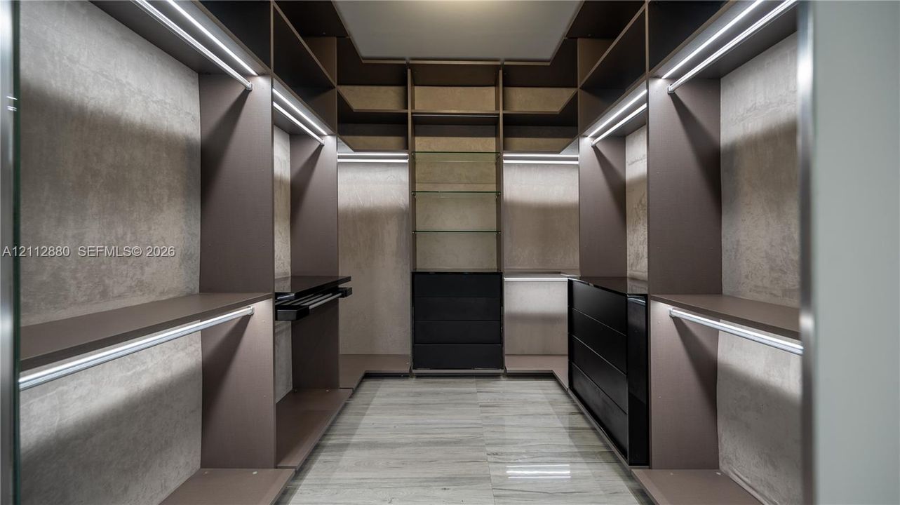 Custom walk-in closet featuring extensive built-in cabinetry, integrated LED strip lighting, open shelving, a multi-drawer dresser unit