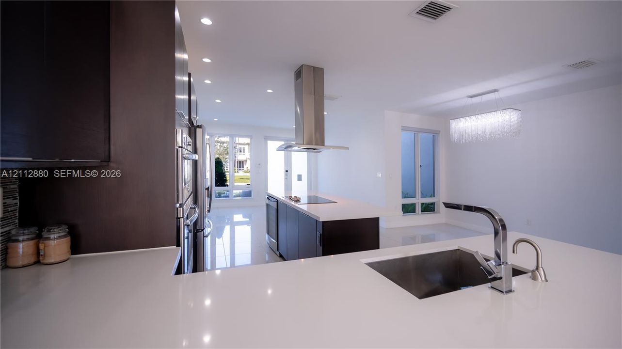Kitchen featuring a center island with a stainless steel range hood, stone-surface countertops, custom flat-panel cabinetry, and integrated stainless steel appliances