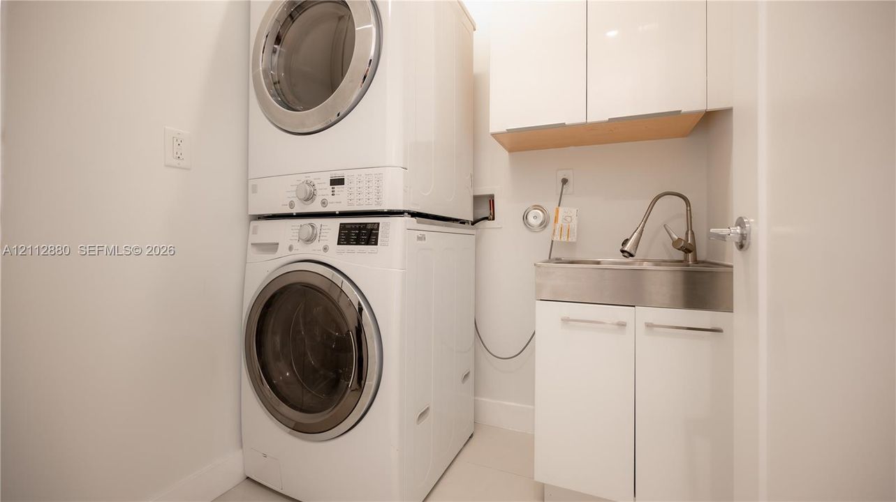 Laundry space featuring a stacked washer and dryer, stainless steel utility sink